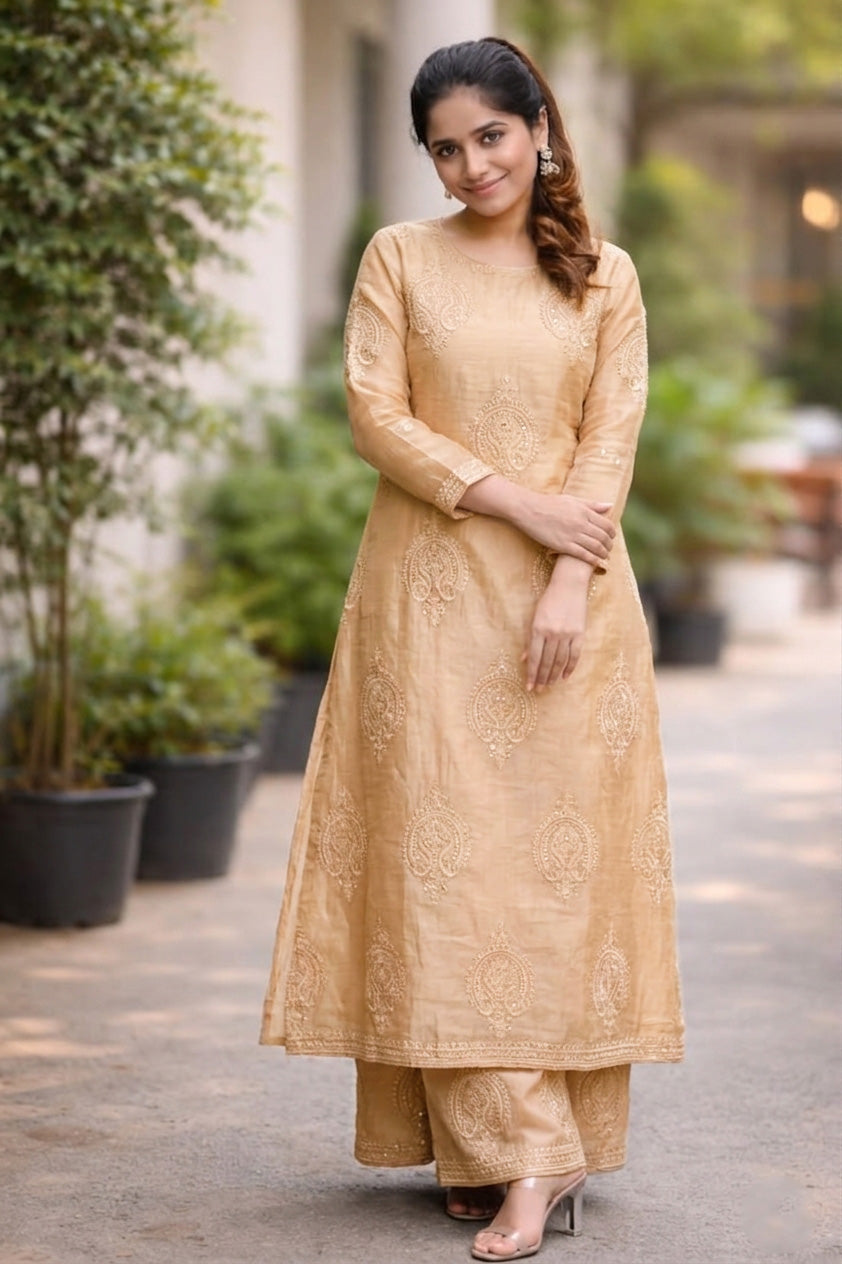 Woman wearing a gold traditional outfit standing outdoors with plants in the background
