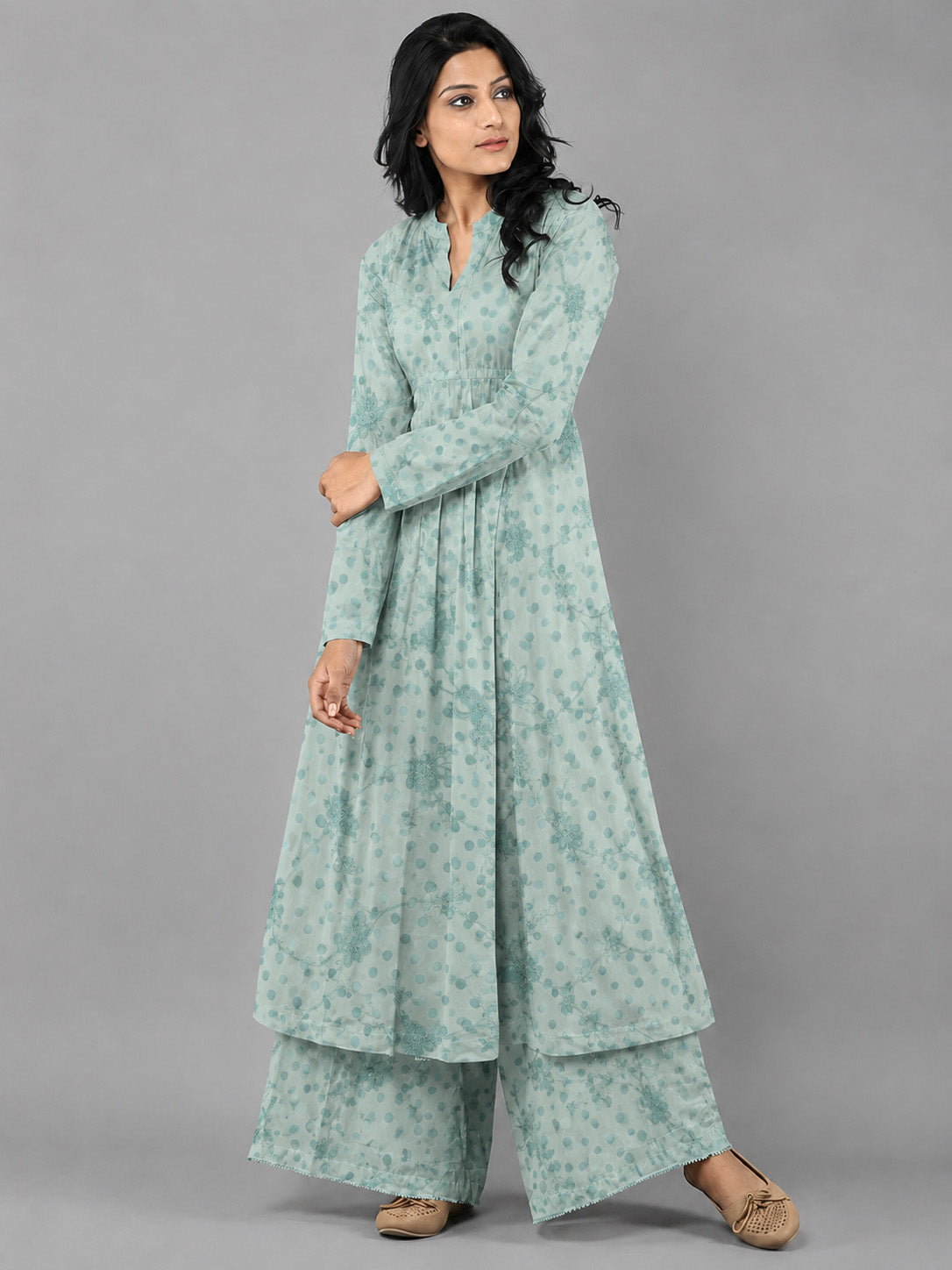 Woman wearing a long, light green dress with a pattern on a gray background