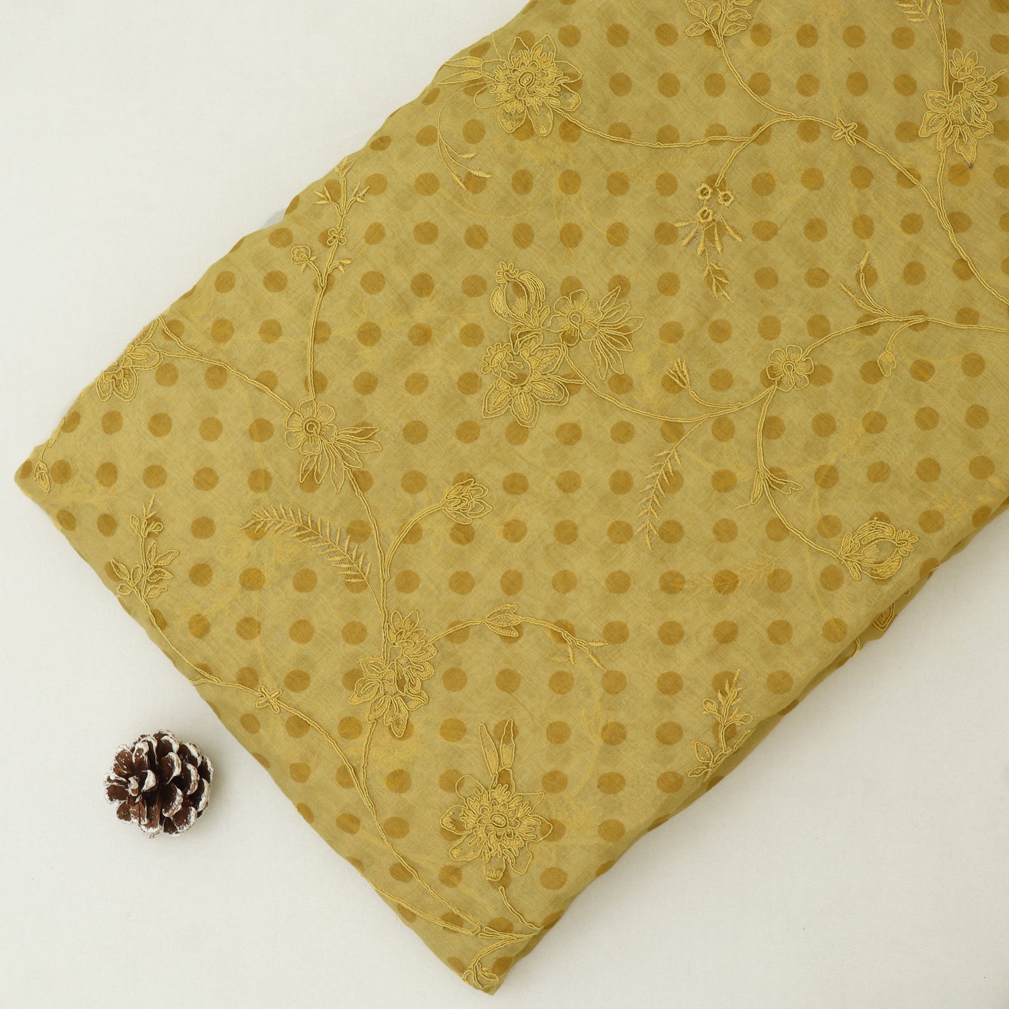 Gold embroidered fabric with a pine cone on a white background